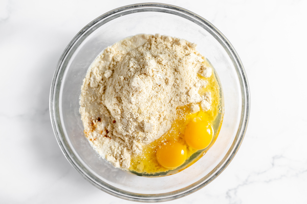 Image, taken from above shows a glass bowl with eggs with the dry ingredients for blackberry scones