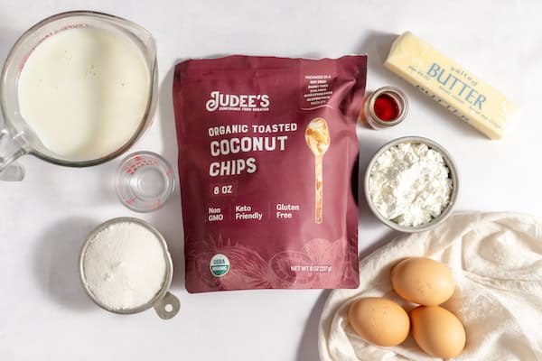 Photo, taken from above, shows ingredients for coconut pudding on a counter- sugars, eggs, butter, vanilla, coconut chips and more. 