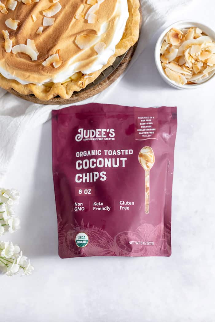 Image, taken from above, shows part of a coconut cream pie with meringue, next to a bag of Judee's organic toasted coconut chips.