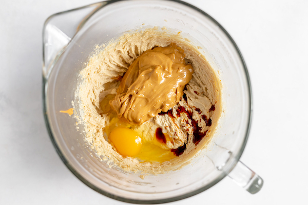 Image shows a glass mixing bowl with the peanut butter batter and egg, vanilla and peanut butter added, ready to be mixed.