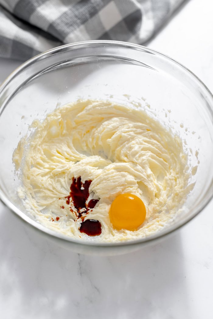 Image shows a glass bowl with butter and sugar beaten, and an egg yolk and vanilla on top.
