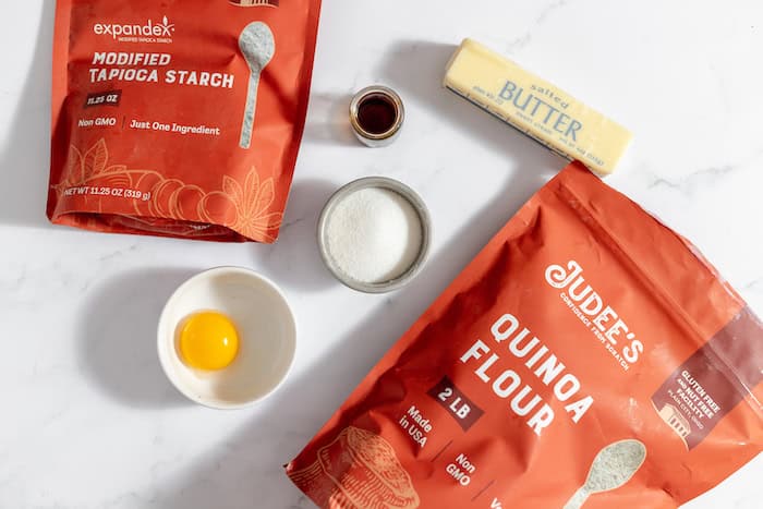 Image shows all the ingredients needed to make gluten free butter cookies- tapioca starch, quinoa flour, butter, an egg, sugar, and seasoning