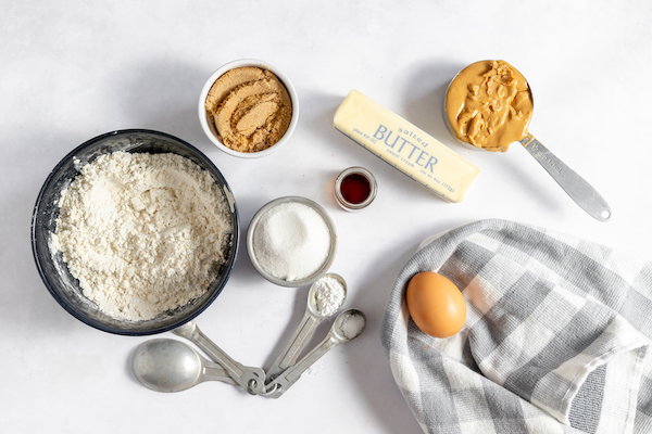 Image shows the ingredients to make gluten free peanut butter cookies- flour, brown sugar, peanut butter, butter, an egg, vanilla and more. 