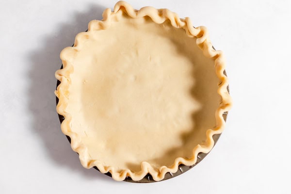 Image, taken from above, shows a pie plate with a gluten free crust placed inside, ready to be baked. 