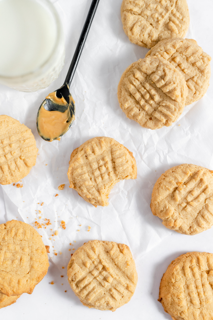 Image shows about ten gluten free peanut butter cookies, freshly baked, with a spoon of peanut butter sitting nearby.