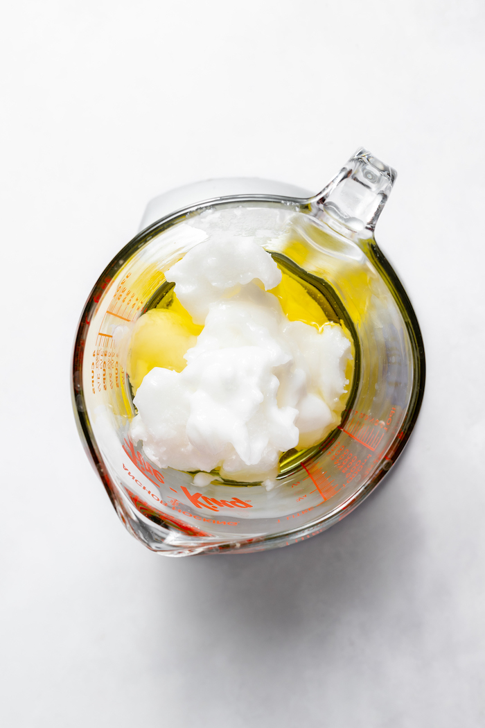 Image shows a glass measuring cup photographed from above with oils and ingredients needed to make soap