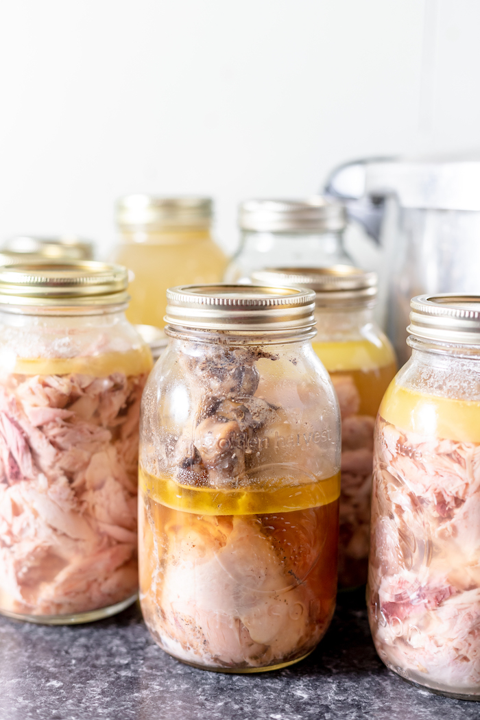 Image shows a large number of glass mason jars on a counter full of chicken and broth.