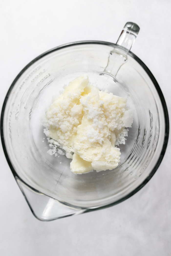 Photo shows a glass measuring cup photographed from above, with lye beads, added to frozen goat milk