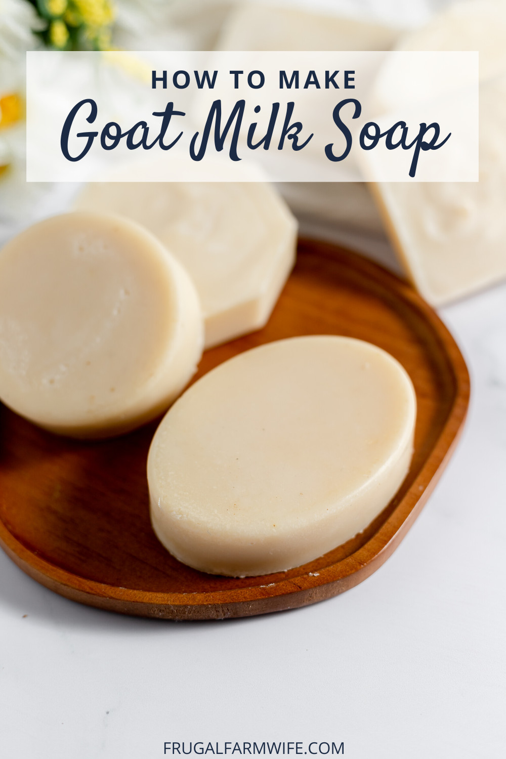 Image shows several bars of goat milk soap on a wooden soap dish sitting on a white counter with text overlay that reads "How to Make Goat Milk Soap"