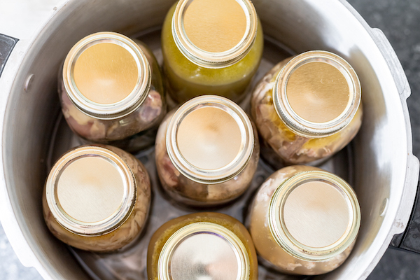 An overhead photo shows seven mason jars with lids arranged inside a large pressure canner pot, ready to be sealed.