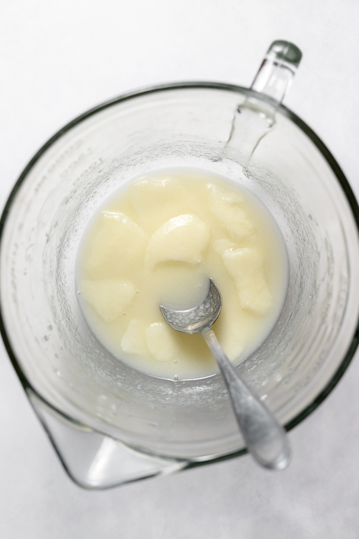 Photo shows a glass measuring cup photographed from above, with a spoon mixing lye with goat milk that is partially frozen