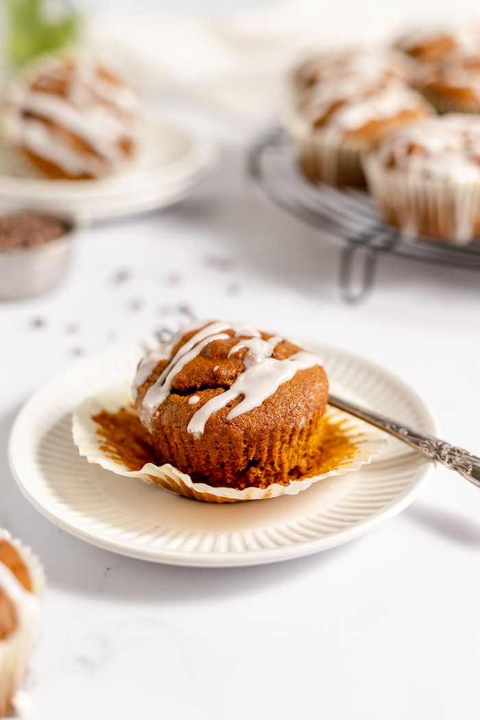 Image shows a gluten free pumpkin muffin, drizzled in vanilla glaze, sitting on a plate with a fork. 