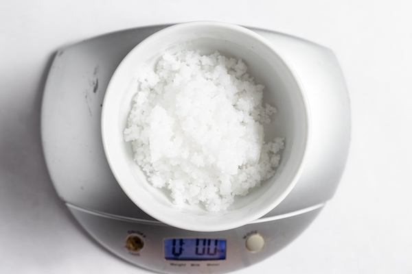 Photo shows a white bowl of lye on a small kitchen scale on a white counter top