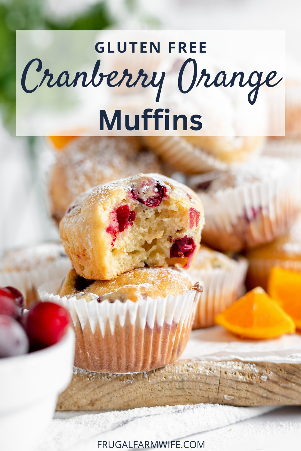 Images shows a stack of gluten free cranberry orange muffins on a counter. The front muffin has a small bite taken out of it. Nearby are orange slices and cranberries with a text overlay that reads "Gluten Free Cranberry Orange Muffins"