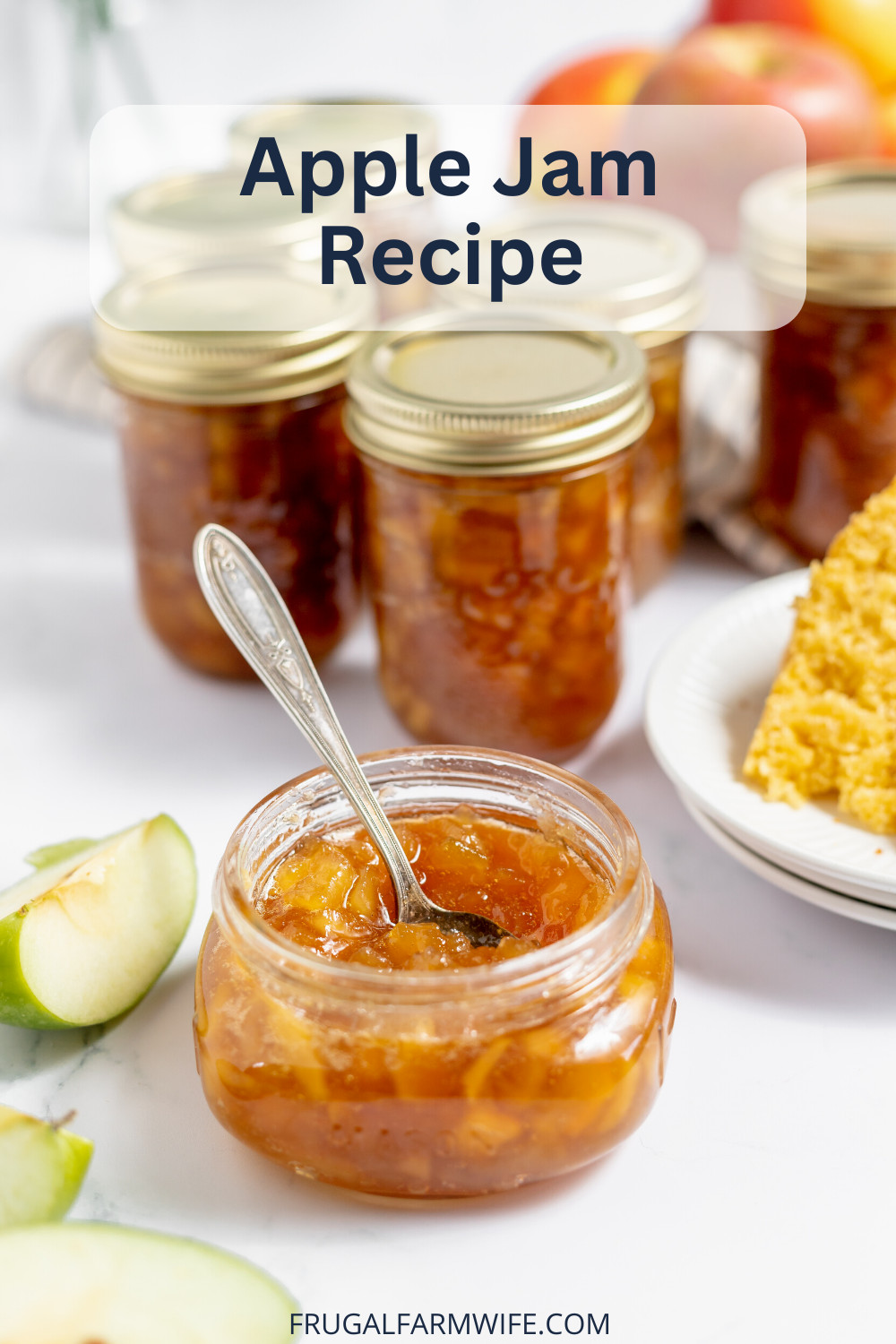 Image shows a small glass jar of apple jam in the foreground with a spoon in it. Behind are several more larger jars of apple jam, with a green apple slice on a table next to them. Overlay text reads "Apple Jam Recipe"