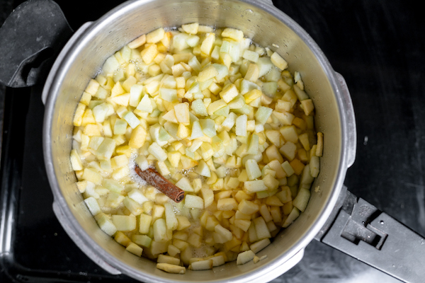 Photo shows a large pot, photographed from above, with apple pieces and a cinnamon stick boiling in water