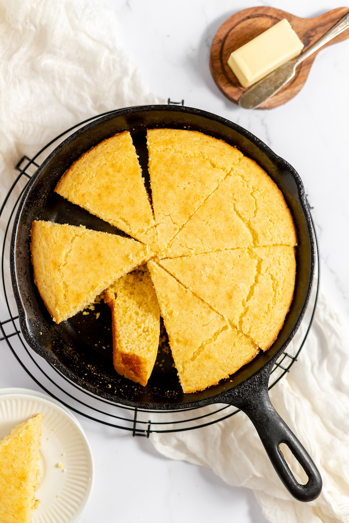 Image, taken from above, shows a cast iron skillet with fresh cornbread cut into slices in it. 