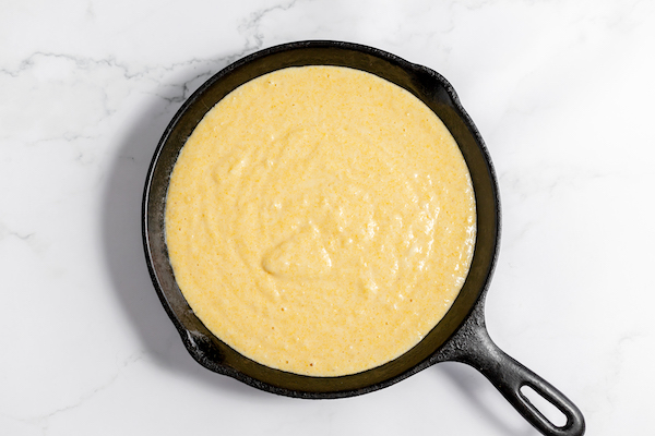 Image, taken from above, shows the cornbread batter poured into a cast iron skillet.