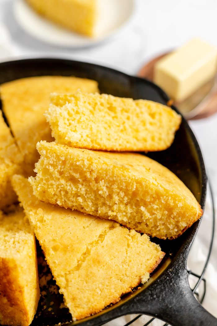 Image shows a close up of slices of cornbread sitting in a cast iron skillet.