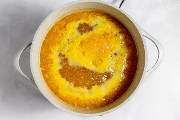 Image shows a large pot of  boiling orange juice, sugar and oranges. 