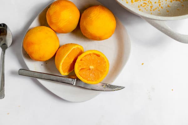 Image shows a white plate of oranges, with one sliced in half. Next to the plate sits a small spoon. 
