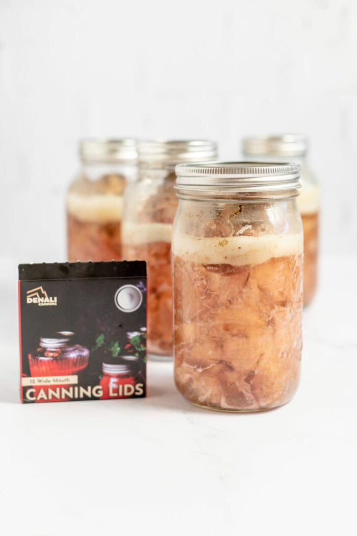 Image shows several jars of pork with Denali canning lids on them.