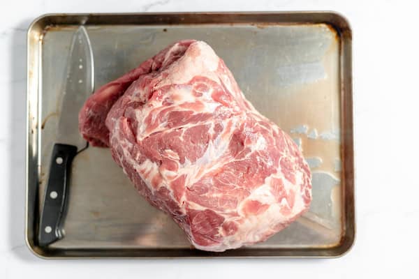Image, taken from above, shows a large pork shoulder roast on a pan. 