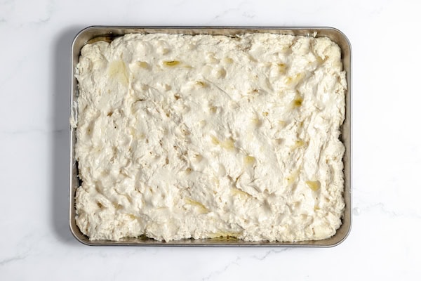 Image, taken from above shows gluten free focaccia dough in a pan, drizzled with olive oil