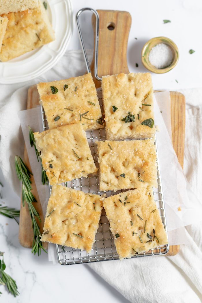 Image, taken from above, shows piece of gluten free focaccia with rosemary and garlic on a cutting board