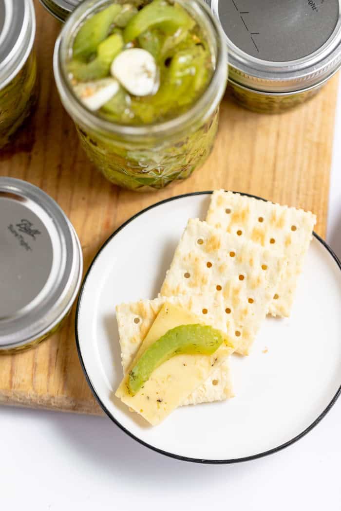 Image shows a small plate with several saltine crackers on it, a piece of pickled celery sits on one cracked. Nearby are several jars of pickled celery, one with the lid off.