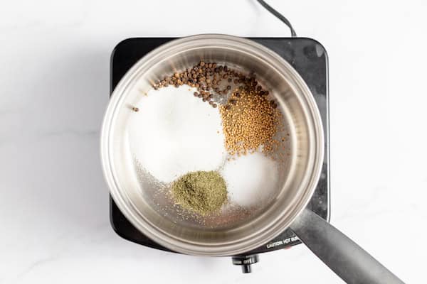Image, taken from above, shows a saucepan on a burner with the spices for pickling in the bottom of the pan.