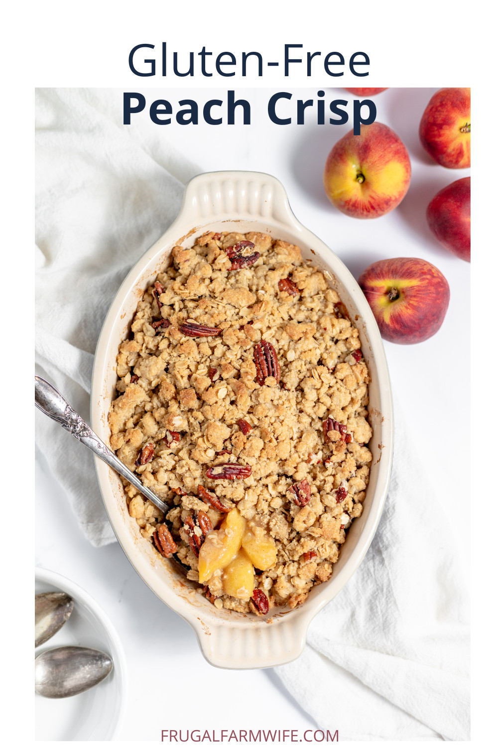 Image, taken from above, shows a ceramic oval pan with gluten free peach crisp in it. A spoon sits in the dish to serve it, with several peaches next to it on the table. 