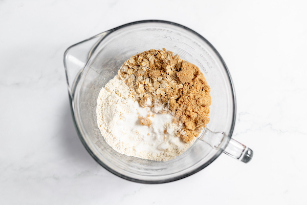 Image, taken from above, shows brown and white sugar and oats in a glass bowl.