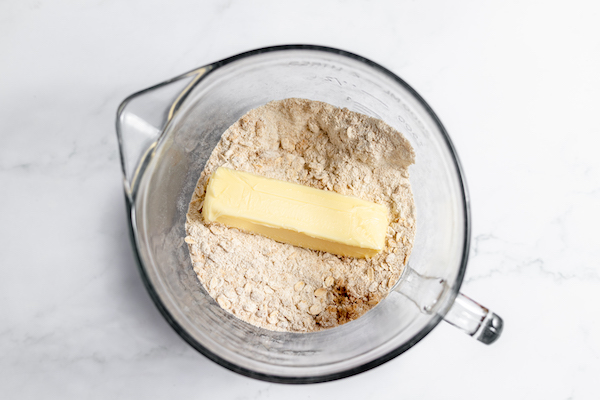 Image, taken from above, shows a stick of butter added to the dry ingredients to make peach crisp