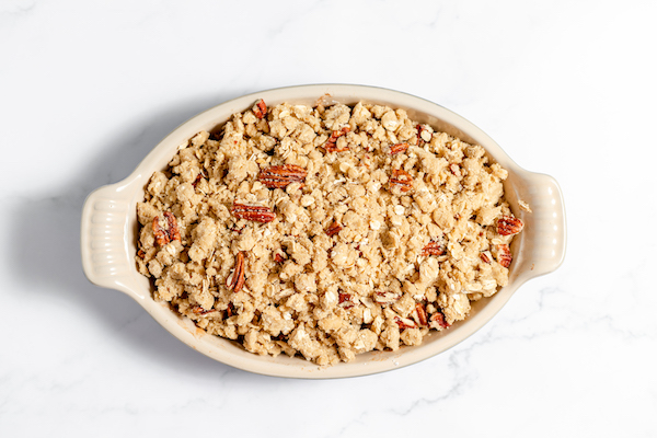 Image, taken from above, shows the gluten free crumble topping sprinkled on the peaches in a ceramic dish. 