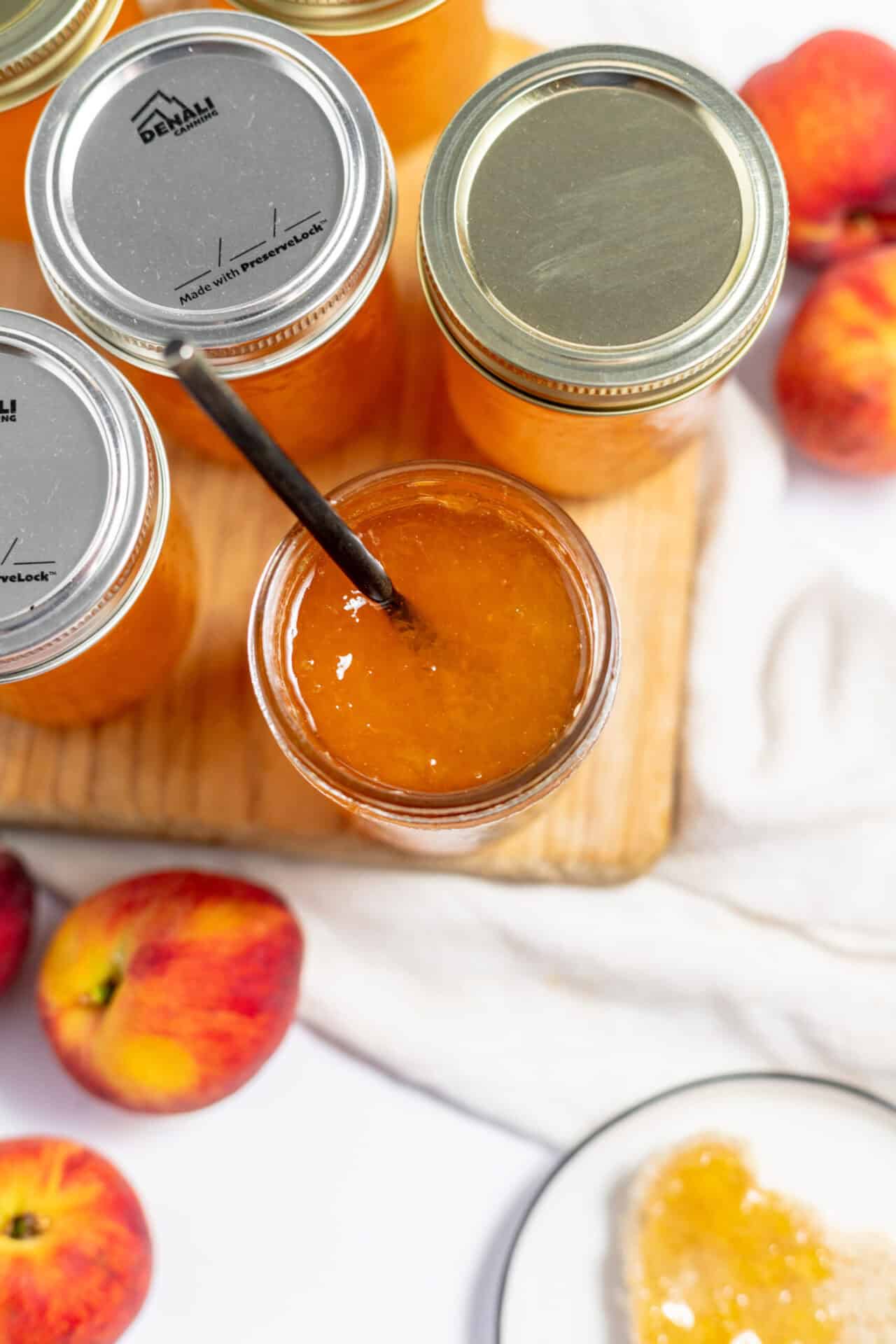 Image shows several cans of peach jam with a spoon in it to serve on toast