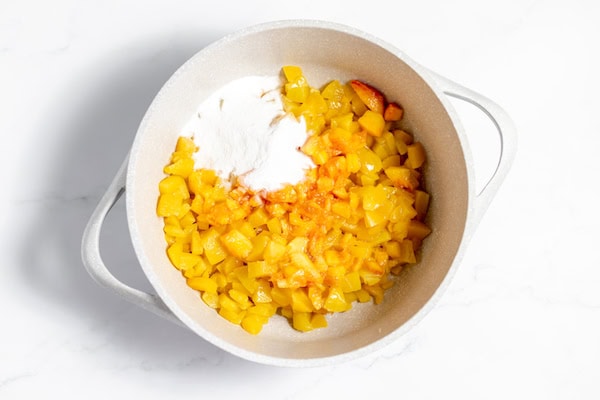 Image, taken from above shows diced peaches, lemon juice, and fruit pectin in a kettle.