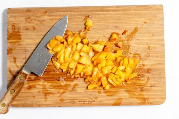 Image, taken from above, shows a knife dicing peaches for making jam