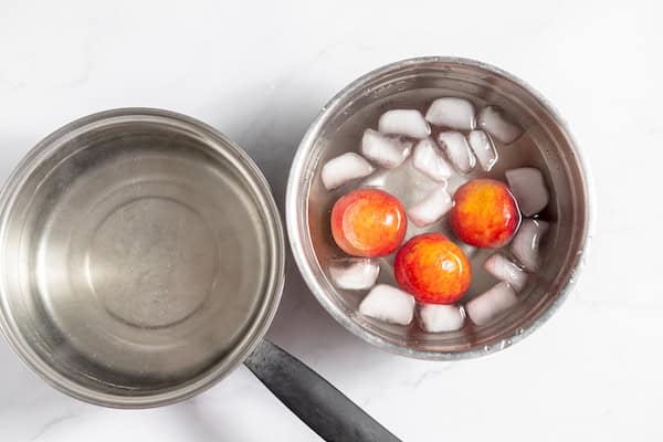 Image, taken from above, shows peaches in a ice bath to cool and stop the cooking process.