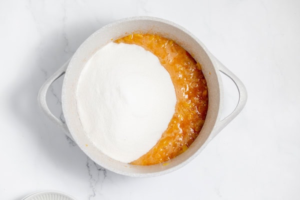 Image shows cooked peaches with sugar in a large pot. 