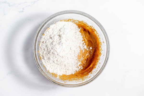 Image, taken from above, shows the dry ingredients for gluten free gingerbread cookies being sprinkled on top of the blended wet ingredients. 