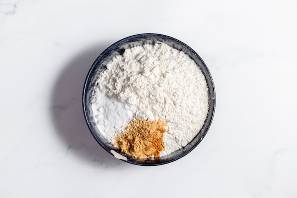 Image, taken from above, shows the gluten free flours in a black bowl with cinnamon and ginger