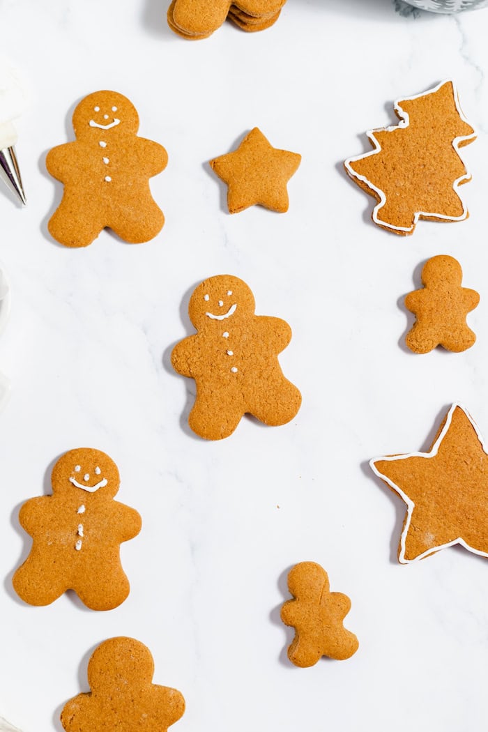 Image, taken from above, shows gingerbread cookies on a white counter top, with an icing bag nearby. 
