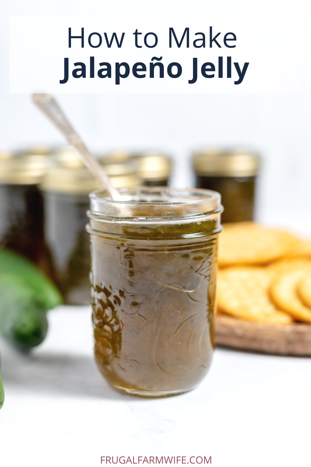 Image shows a glass jar of jalapeno jelly with a spoon in it at the front, with several blurred jars of jelly behind it. Text above reads "How to Make Jalapeno Jelly"