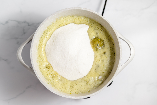 Image, taken from above, shows a pan with sugar being added to the jalapeno jelly mixture.