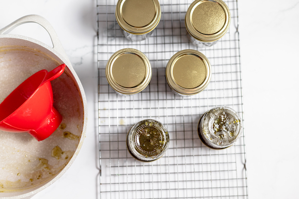 Image, taken from above, shows jars of jalapeno jelly cooling on a cooling rack after being pressure cooked. 