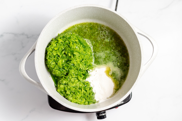 Image, taken from above, shows pureed jalapeño peppers in a pan with pectin and vinegar.