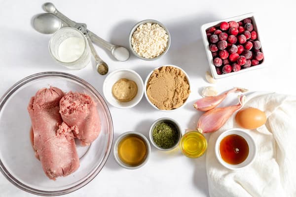 Image, taken from above, shows several bowls laid out with all the necessary ingredients for making cranberry meatballs.