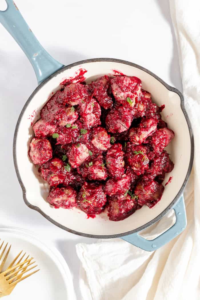 Image, taken from above, shows a skillet full of cranberry meatballs covered in the cranberry barbeque sauce. 