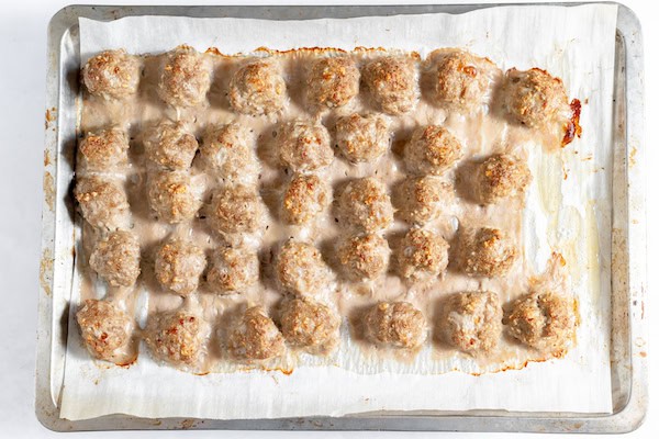 Image, taken from above shows baked meatballs on a lined cookie sheet